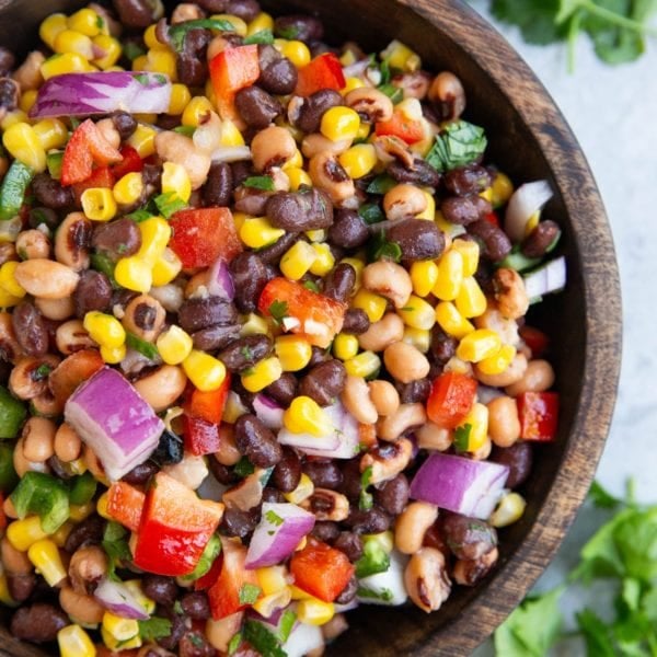 Wooden bowl full of cowboy caviar with a lime and fresh cilantro to the side.