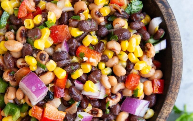Wooden bowl full of cowboy caviar with a lime and fresh cilantro to the side.