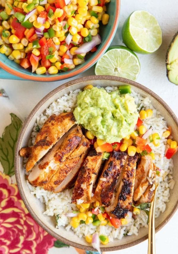 Burrito bowl with cilantro lime rice, guacamole, corn salsa, and chipotle chicken with a bowl of corn salsa to the side.