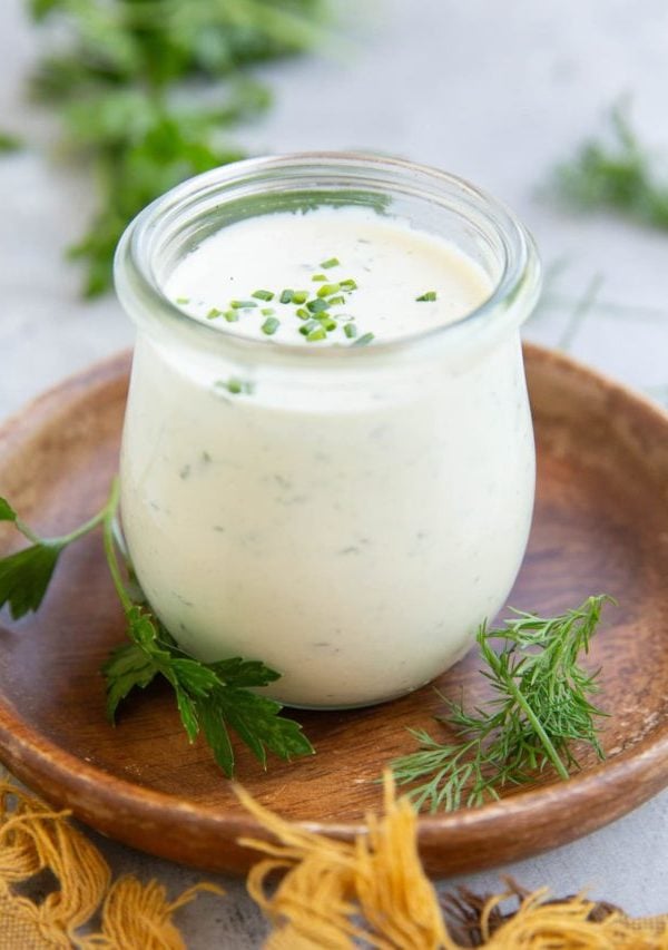 Jar full of homemade ranch dressing with fresh herbs all around.