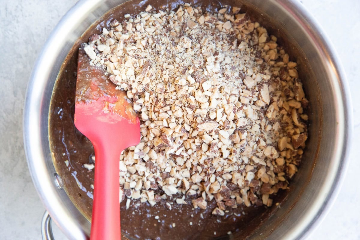 Chopped nuts on top of wet mixture in a saucepan, ready to be mixed in for no-bake cookies.