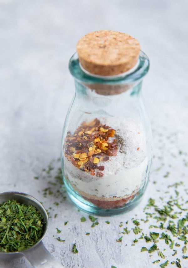 Dry rub for beef in a small glass jar with a top on it. Dried oregano to the side.