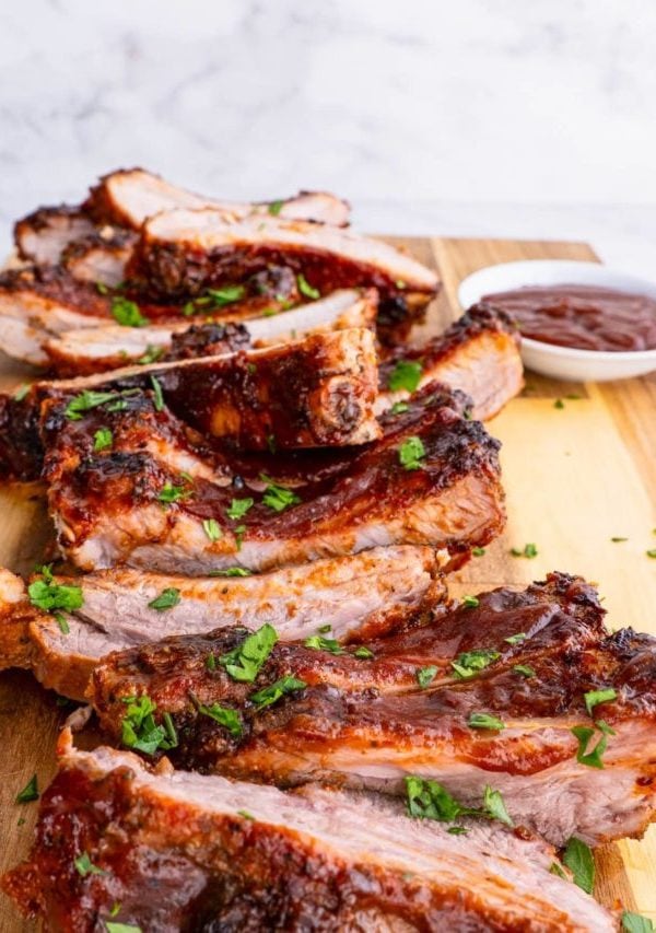 BBQ ribs cut up on a cutting board with bbq sauce and sprinkles of parsley