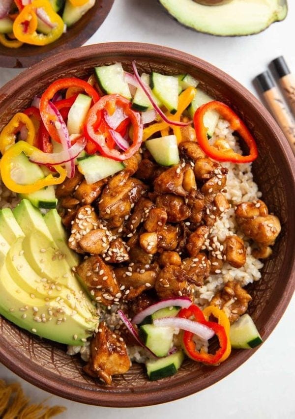 Ceramic bowl full of rice, chicken, pickled vegetables, and avocado slices.