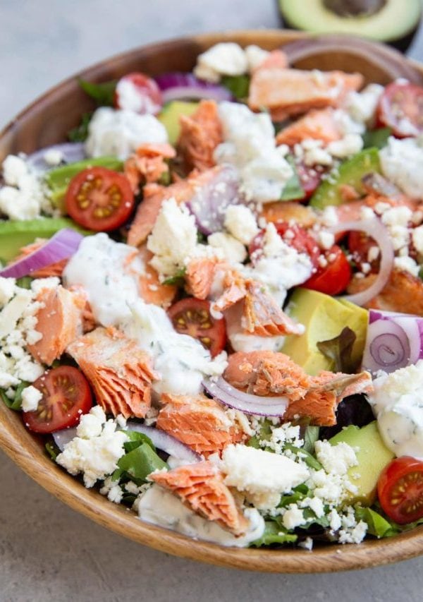 Big bowl of salmon salad with avocado in the background.