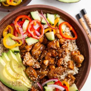 Ceramic bowl full of rice, chicken, pickled vegetables, and avocado slices.
