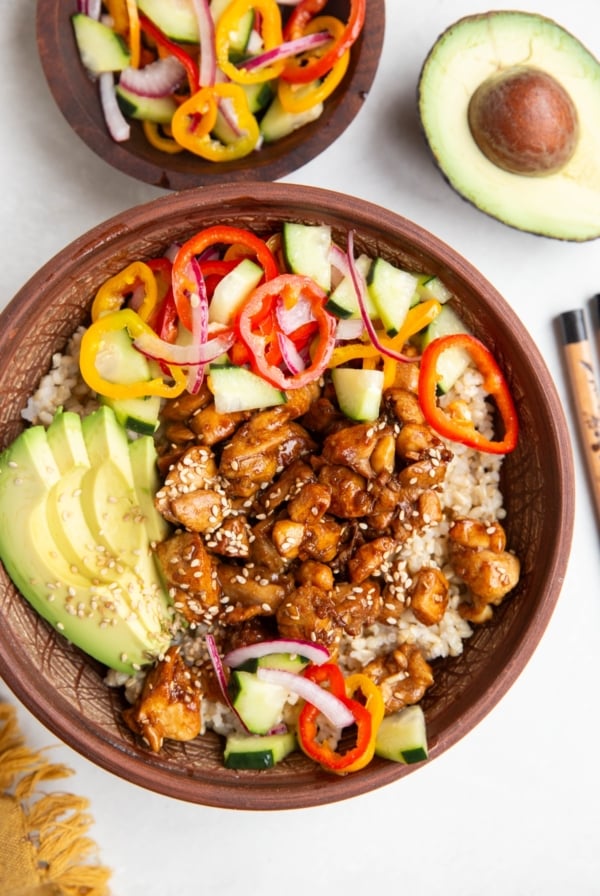 Chicken and rice bowl with pickled vegetables and avocado with a bowl of pickled veggies to the side and chop sticks.