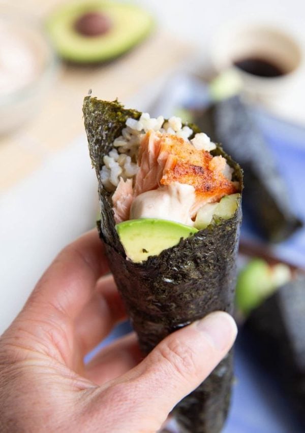 Hand holding a salmon hand roll, ready to eat.