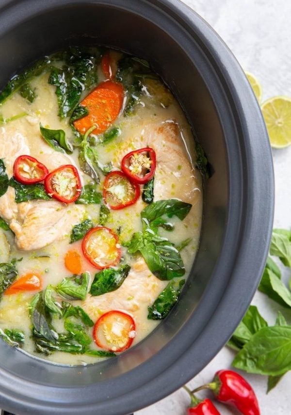 Crock pot full of chicken and sauce with basil and red chilies on top.