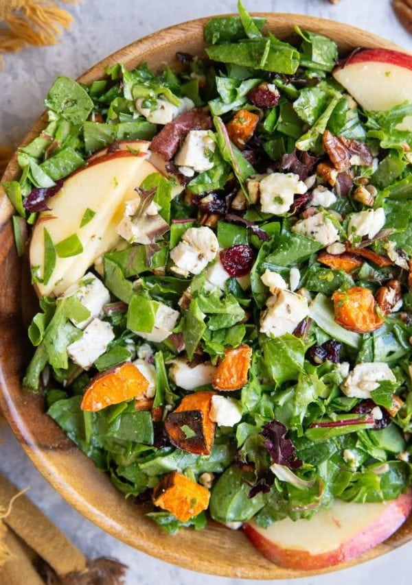 Wooden bowl of chicken and sweet potato salad with a napkin and pecans to the side.