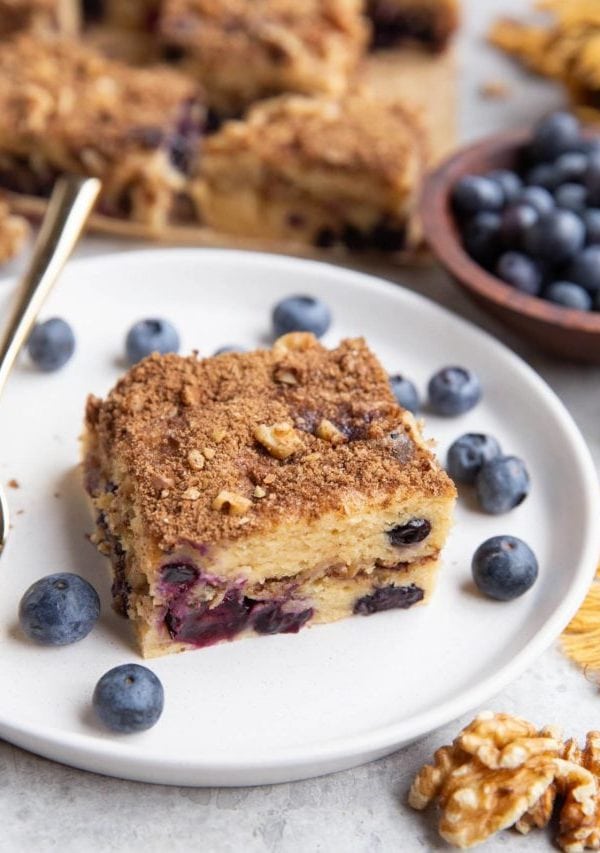 Slice of Greek yogurt coffee cake on a plate with the rest of the coffee cake in the background.