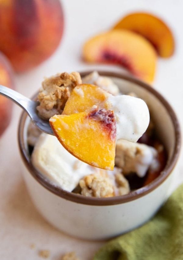 Spoon holing a scoop of peach cobbler with ice cream.