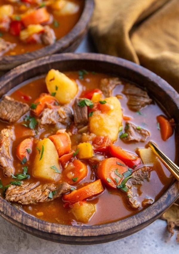 Two wooden bowls of goulash with a gold spoon, ready to eat