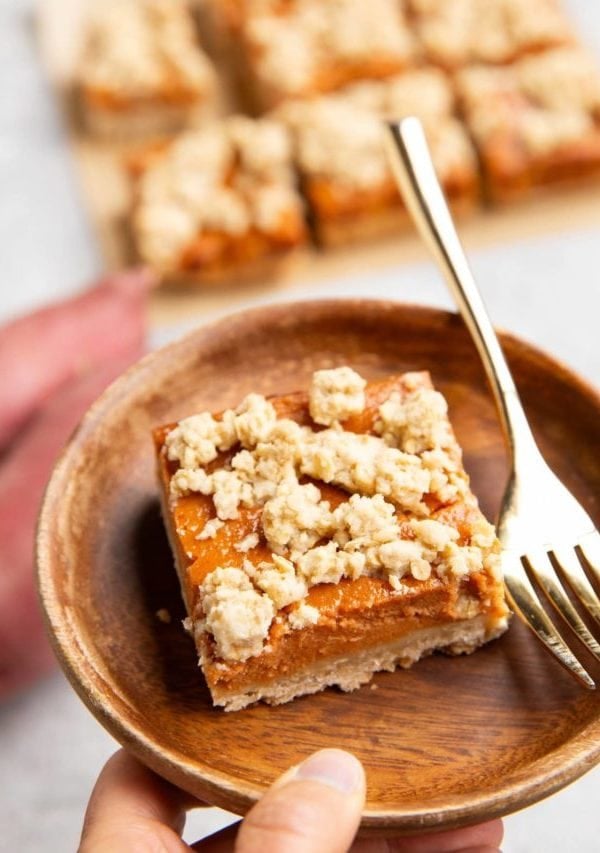 Hand holding a plate with a sweet potato bar and a fork.