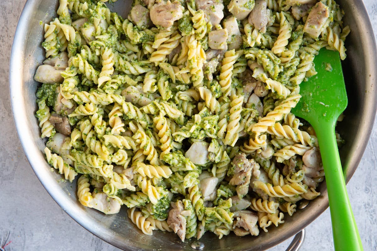 Skillet of chicken pesto pasta freshly mixed together with a rubber spatula.