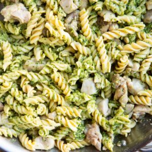 Stainless steel skillet of chicken pesto pasta with a napkin.