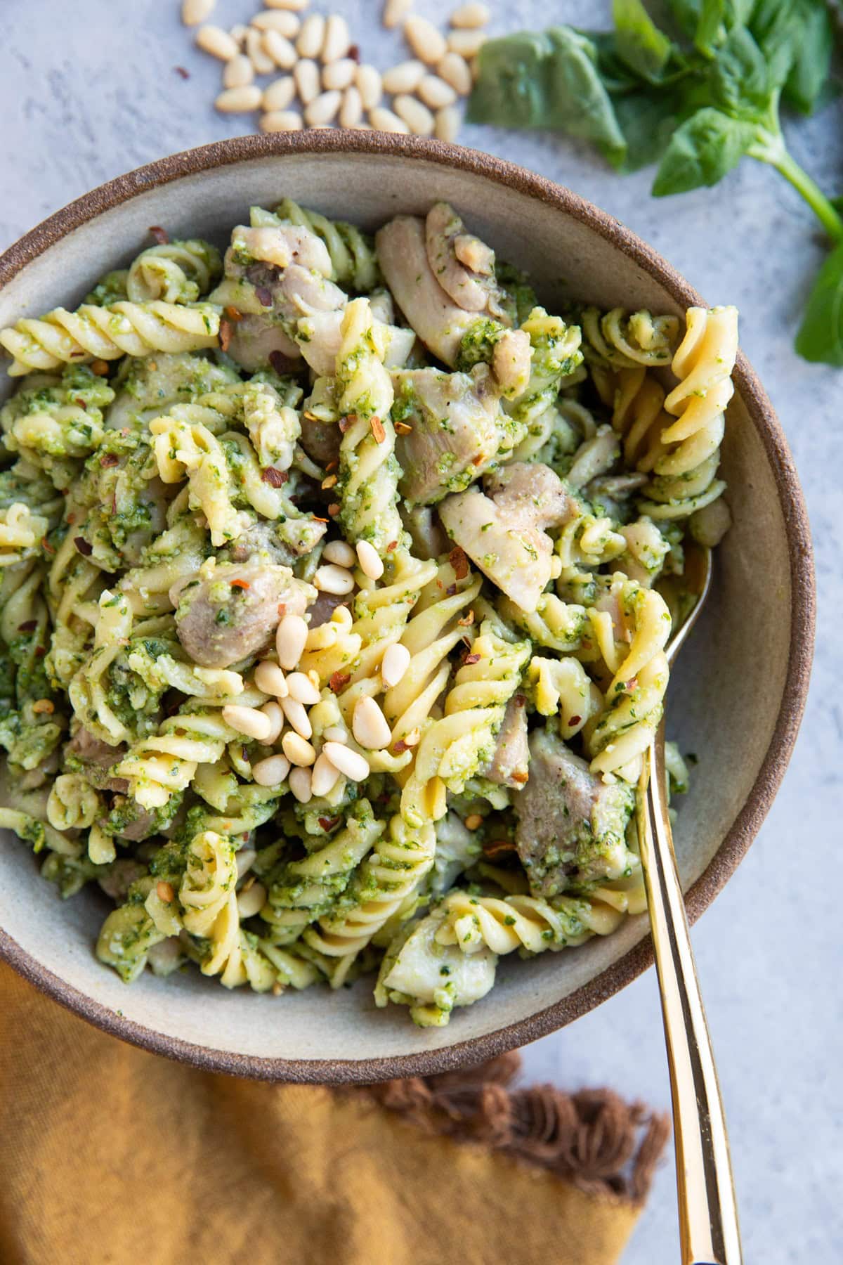 Bowl of chicken pesto pasta with a gold fork, ready to eat.