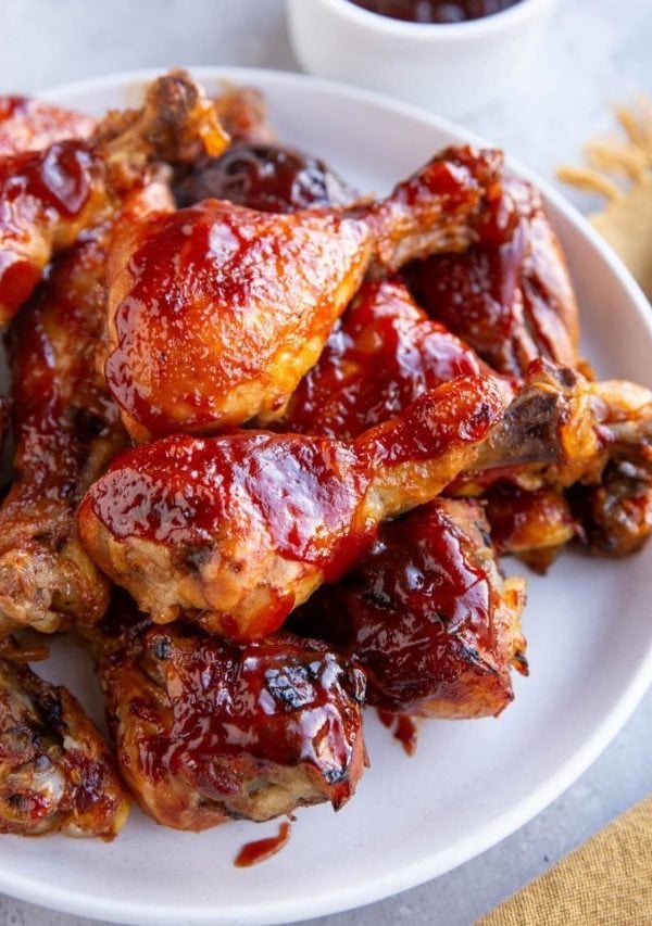 White plate full of chicken drumsticks coated with bbq sauce.
