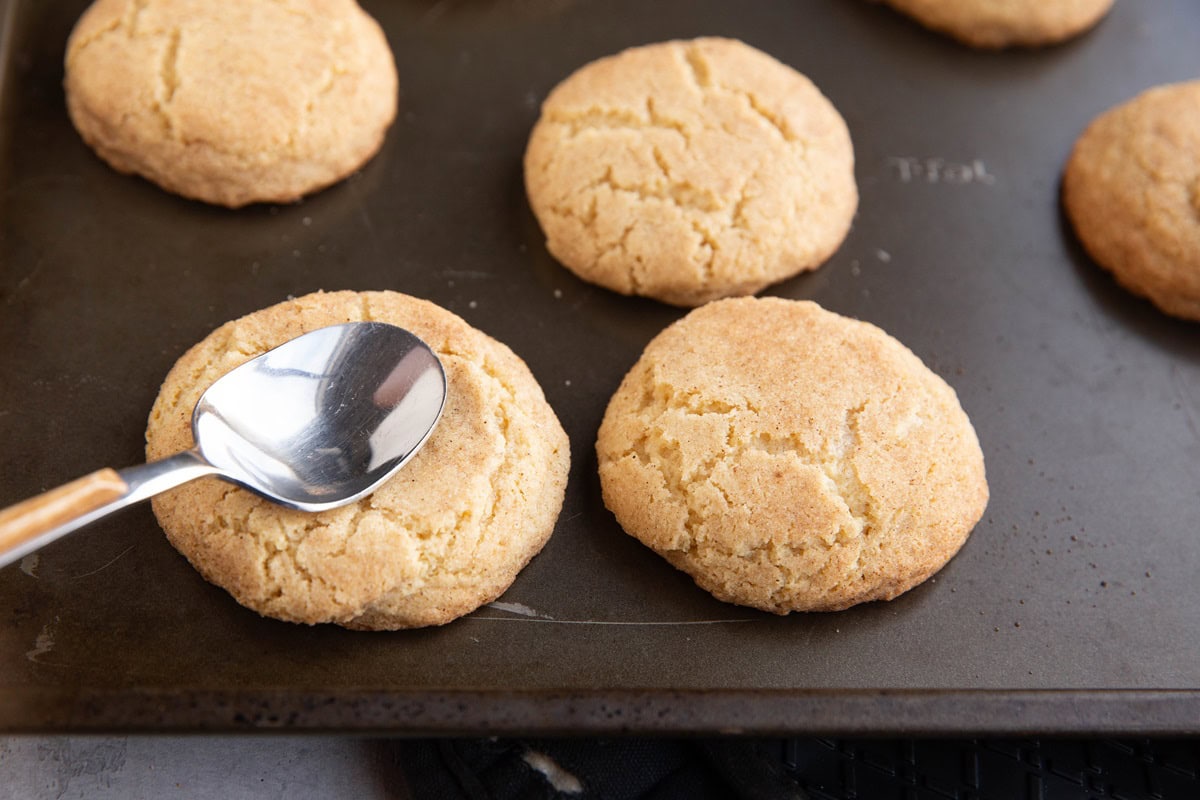 Baking sheet with cookies and a spoon flattening out the center of the cookies.
