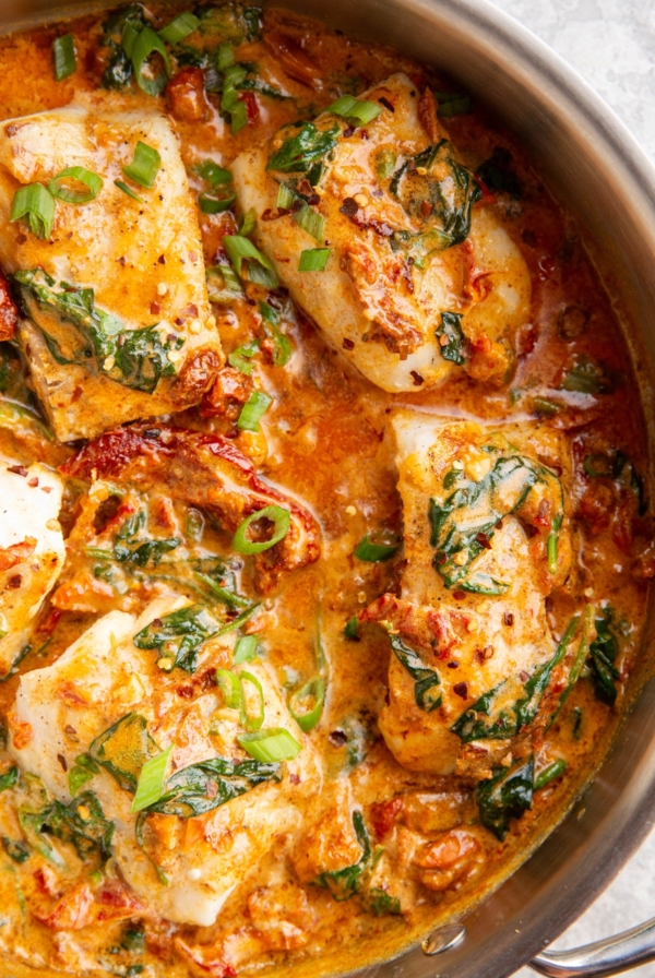 Large skillet full of fish filets covered in creamy sun-dried tomato sauce.