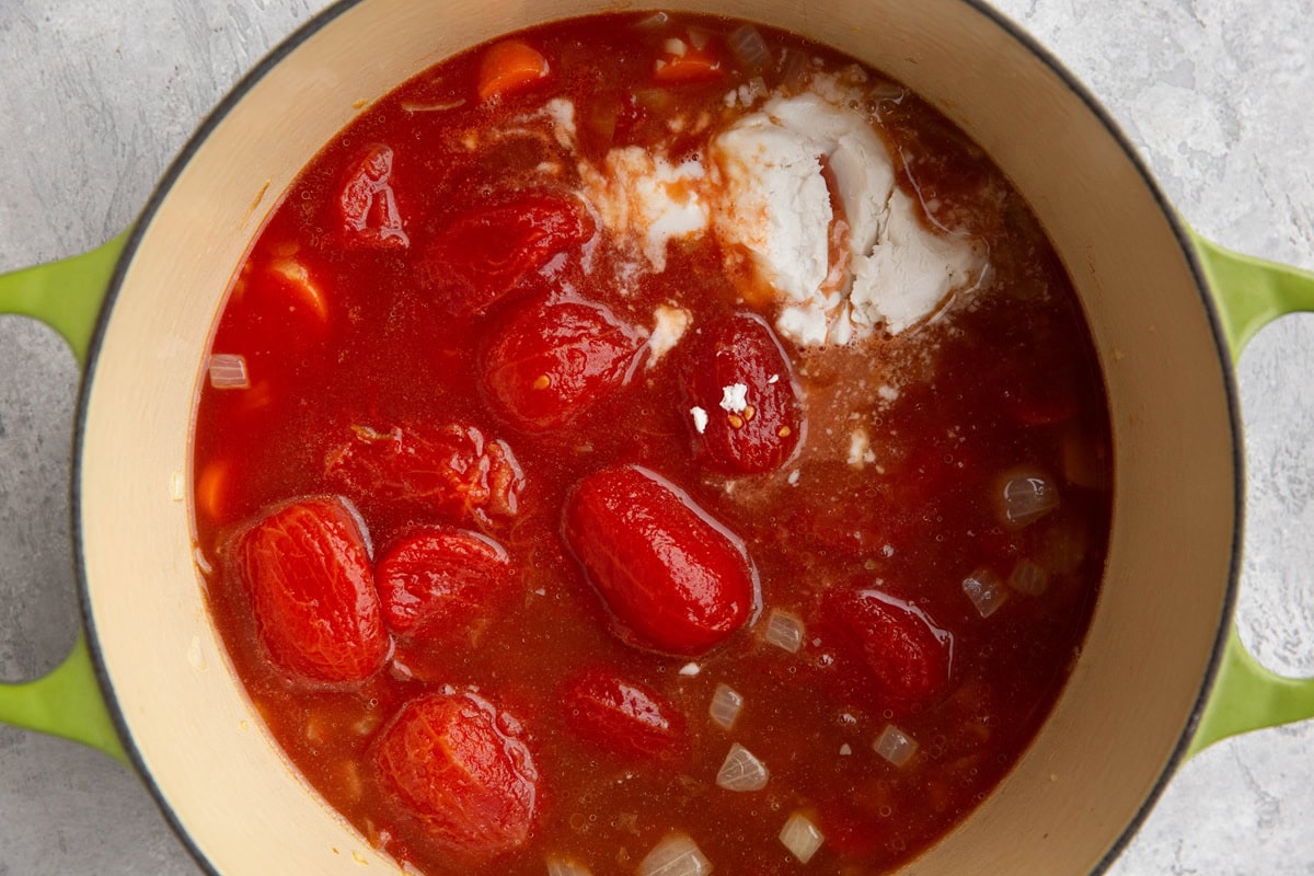 Large pot with tomatoes, broth, onions, and coconut milk inside to make a soup.
