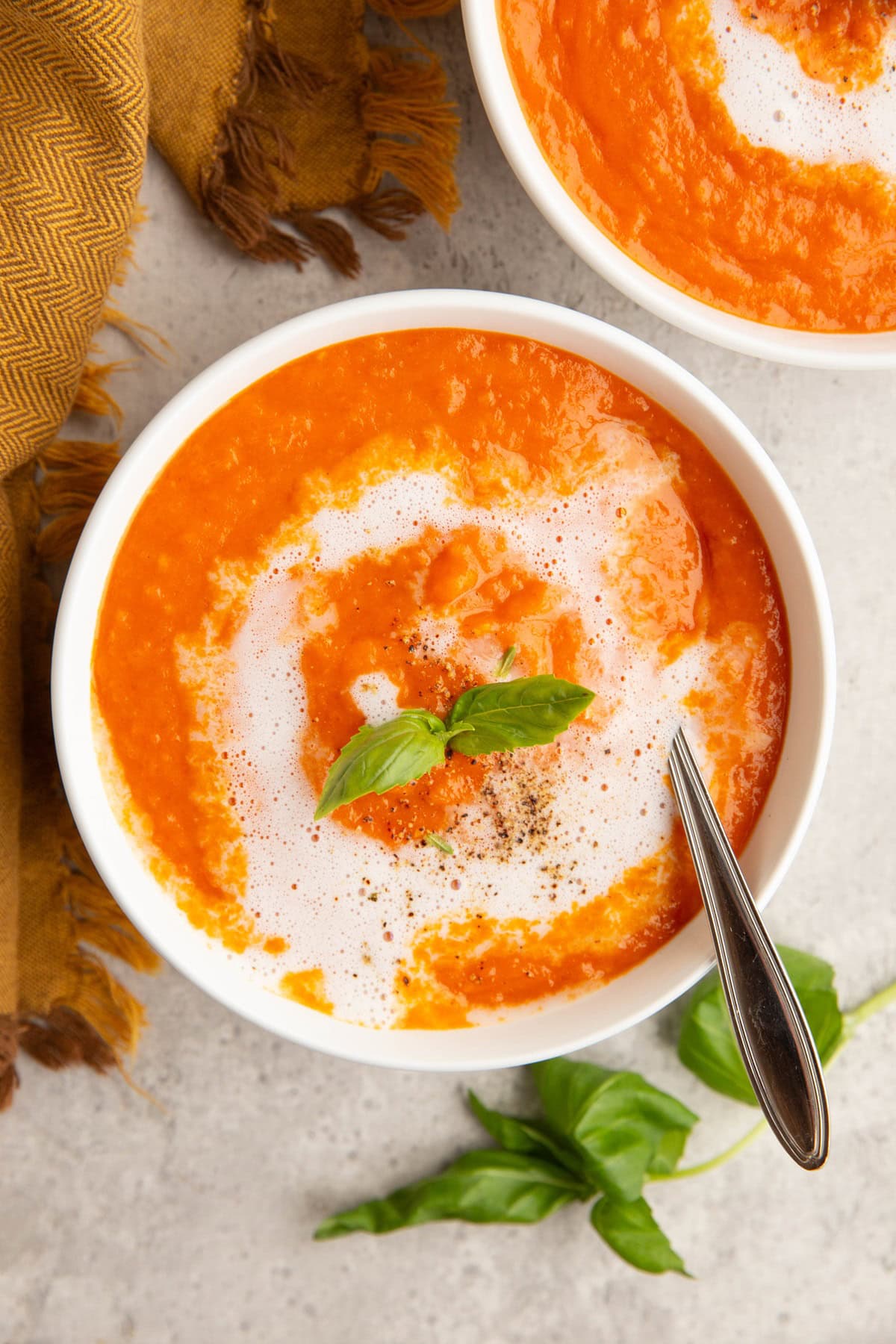 Two bowls of tomato soup with a spoon and fresh basil.