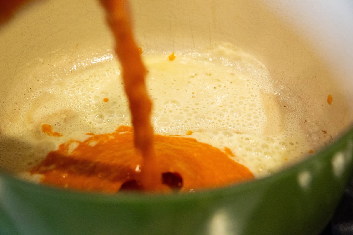 Large pot with roux inside and soup being poured in.