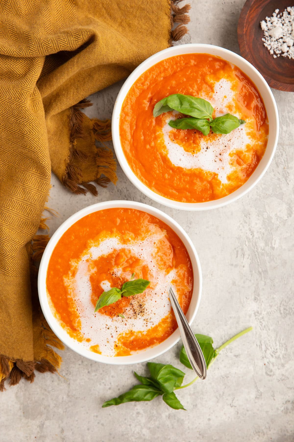 Two white bowls of tomato bisque soup with basil on top.