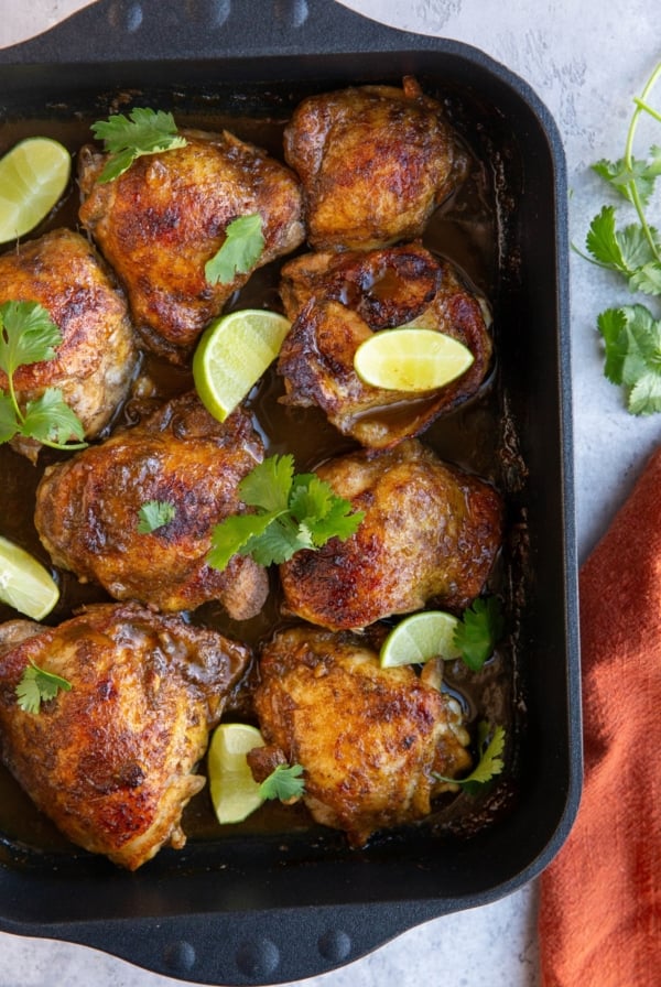 large casserole dish full of baked jerk chicken with lime wedges and cilantro sprinkled on top.