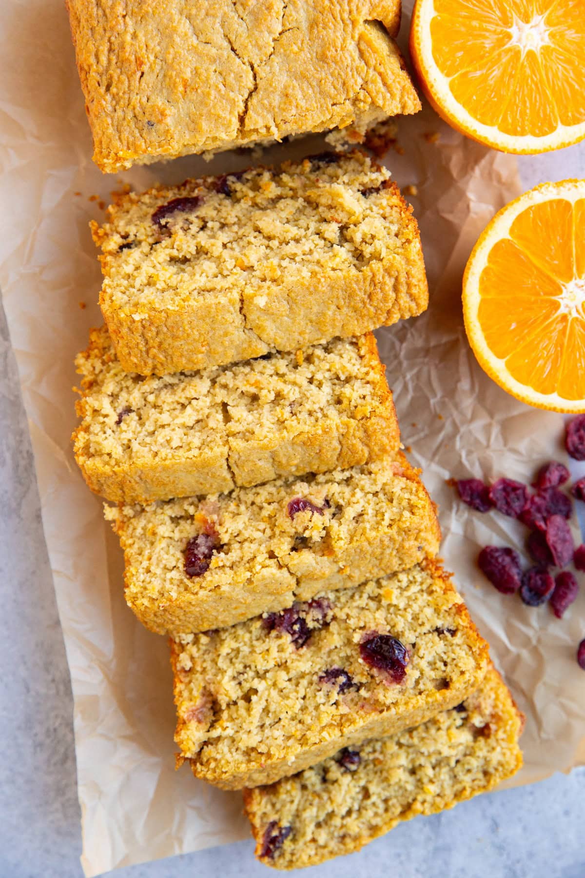 Loaf of cranberry orange bread cut into slices with a halved orange next to the bread and some dried cranberries.