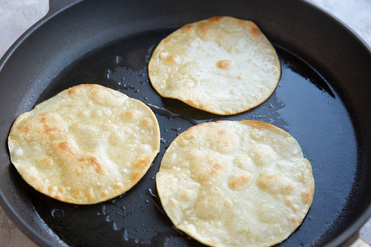 Corn tortillas frying in a skillet