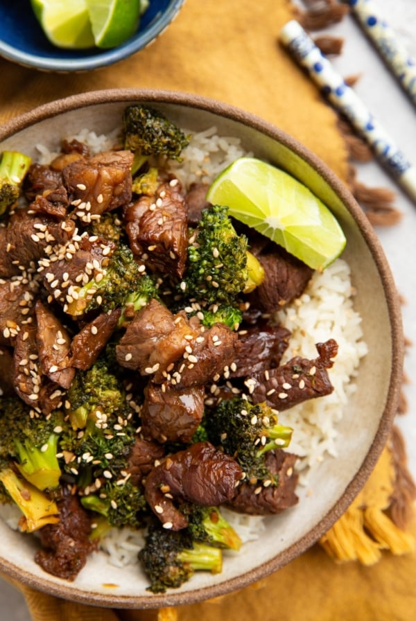 Bowl full of chopped beef, broccoli florets, and rice. Chopsticks and fresh limes to the side.
