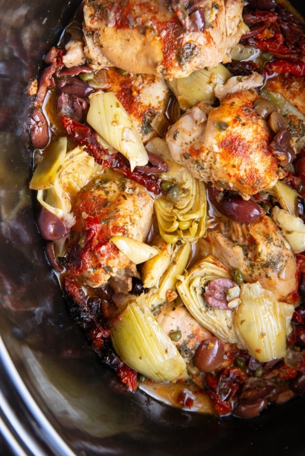 Crock pot full of chicken and Mediterranean ingredients.