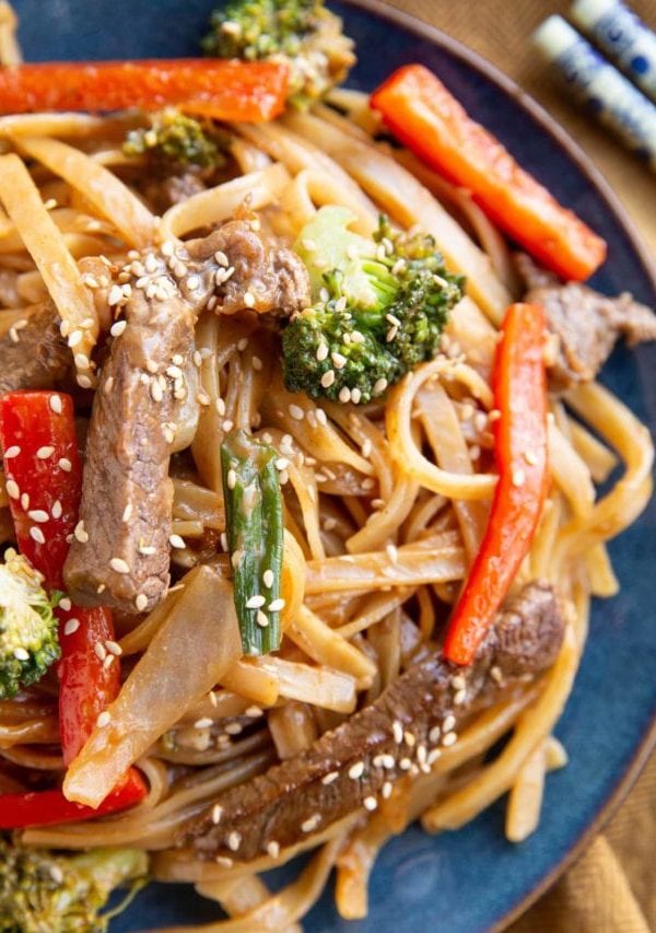 Blue plate with beefy noodles and veggies with chopsticks to the sides.