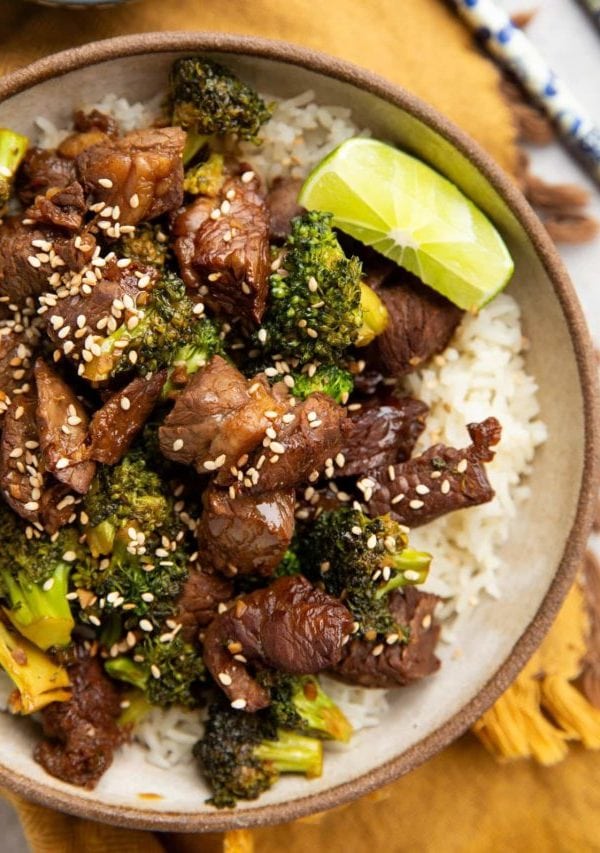 Bowl full of chopped beef, broccoli florets, and rice. Chopsticks and fresh limes to the side.