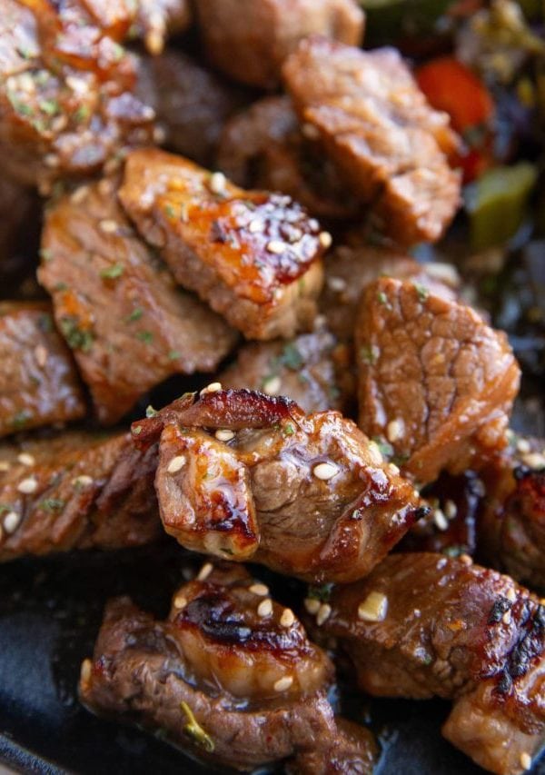 Pile of garlic steak bites on a plate with vegetables.