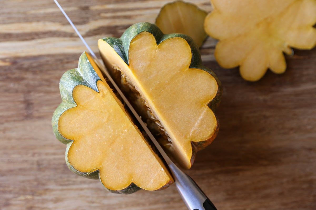 Knife cutting an acorn squash in half through the center.