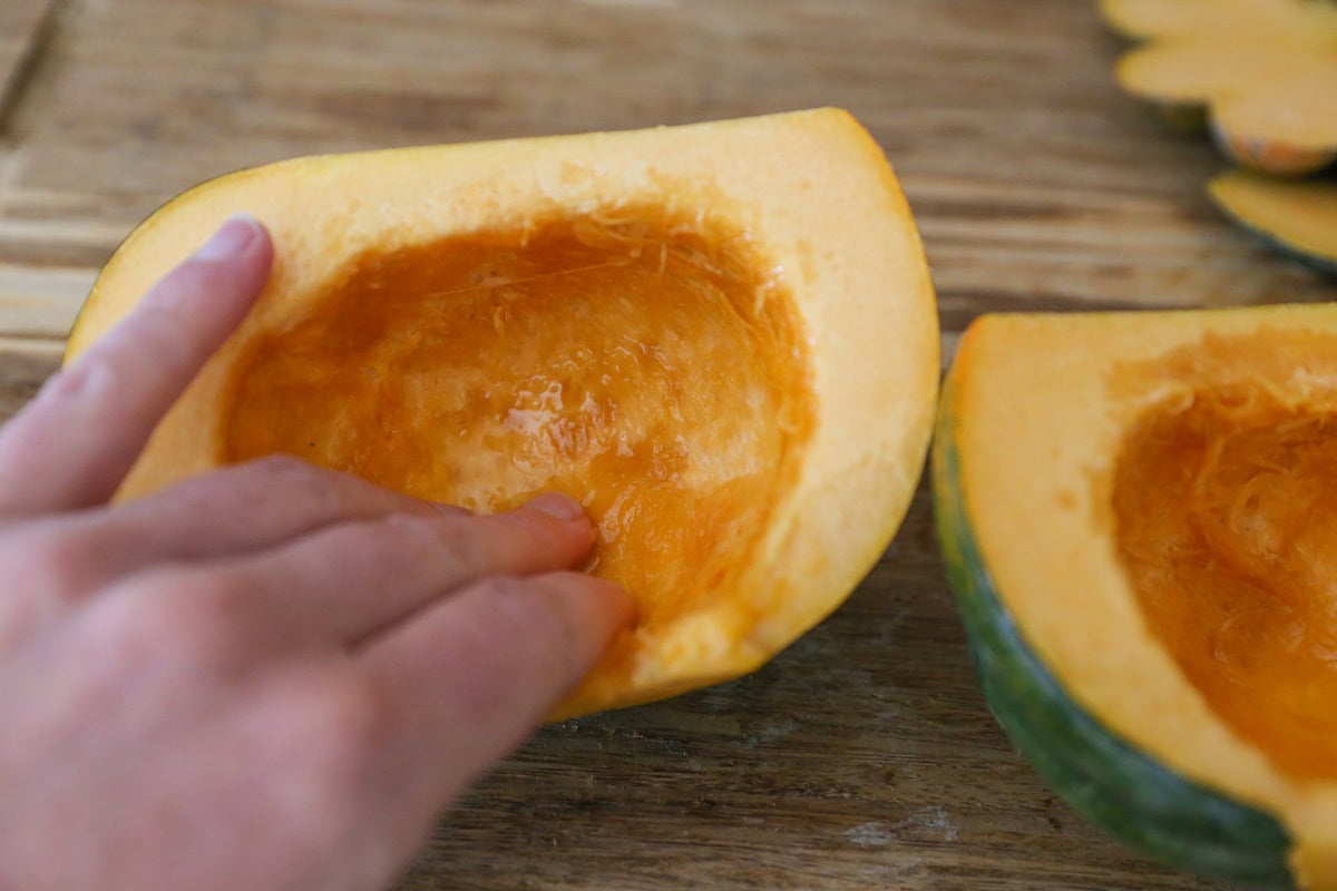 Hand rubbing oil into the flesh of an acorn squash.