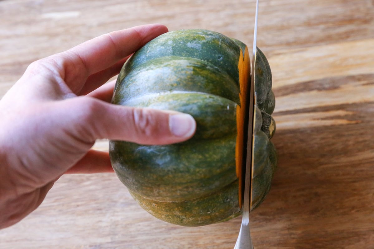 Hand holding an acorn squash and a knife cutting off the tip of the squash.