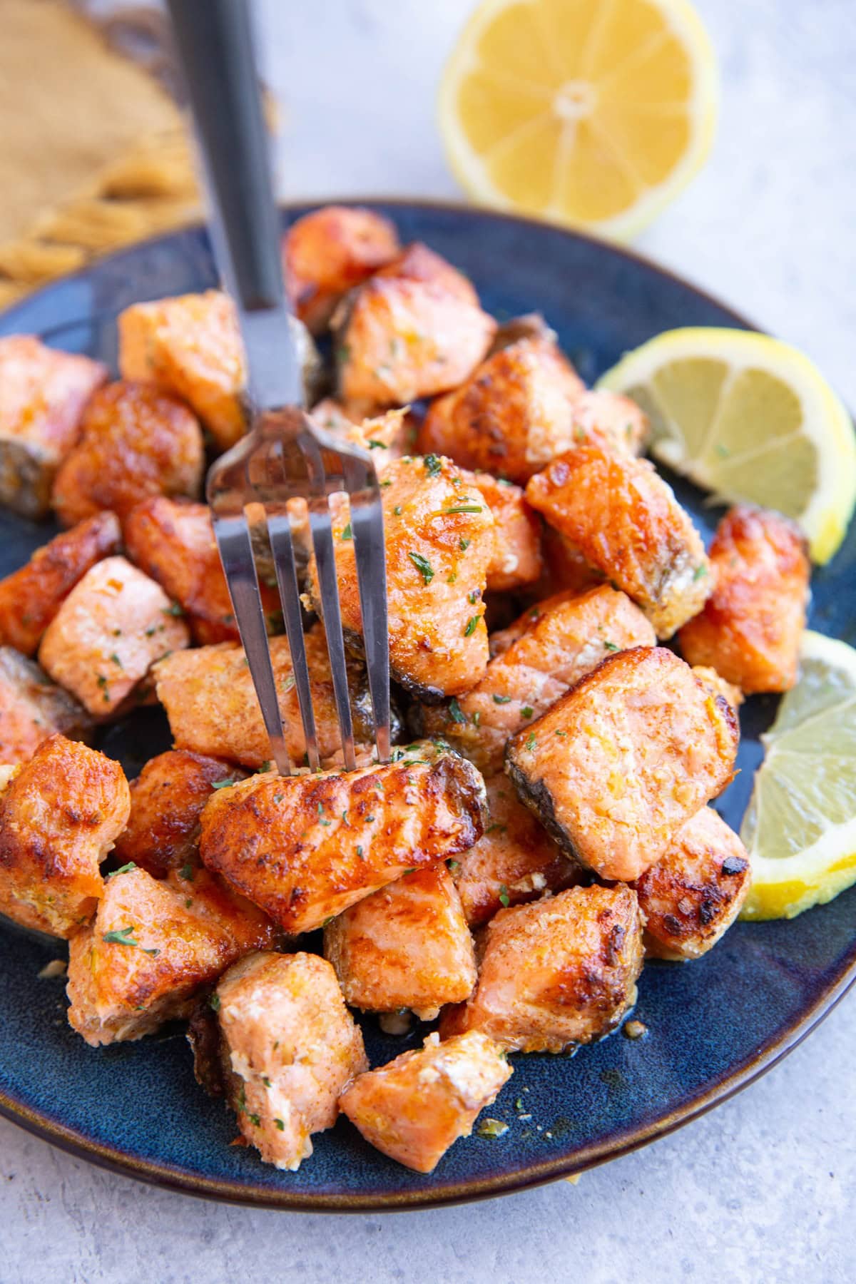 Fork sticking into one of the salmon bites on a plate, to take a bite.
