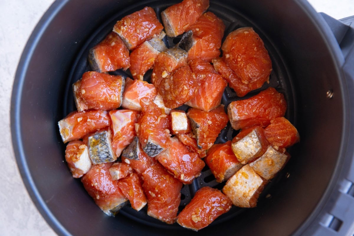 Raw salmon in an air fryer basket, ready to be cooked.