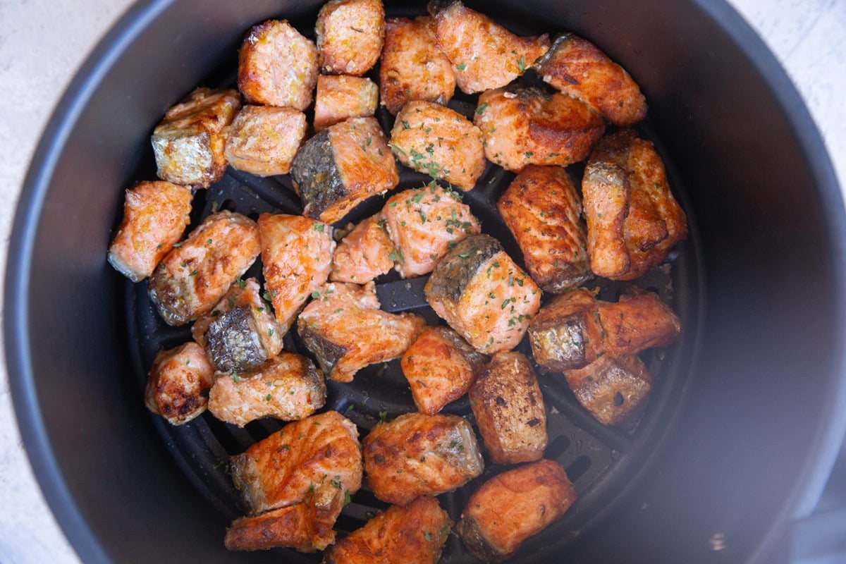 Air fryer basket with cooked crispy salmon bites inside.