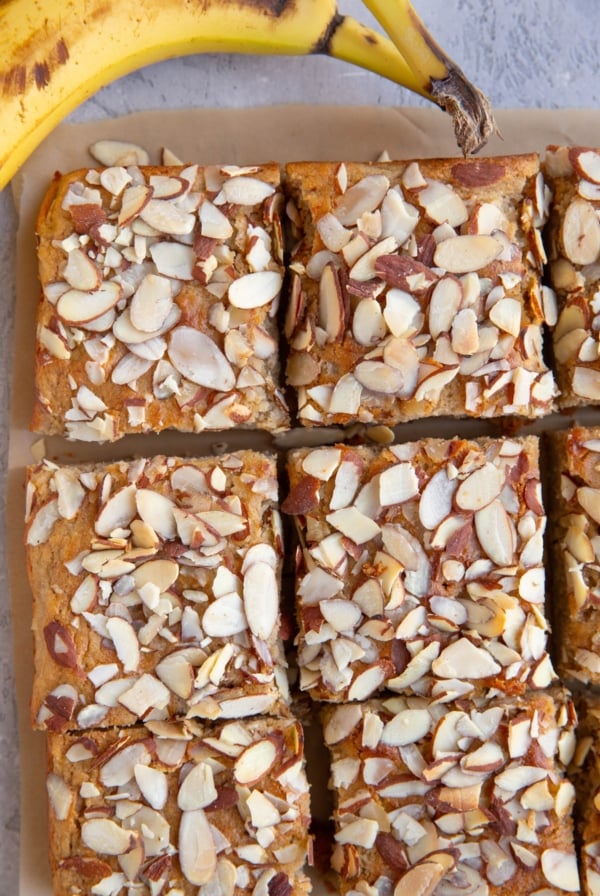 banana cake cut into individual slices with ripe bananas to the side.