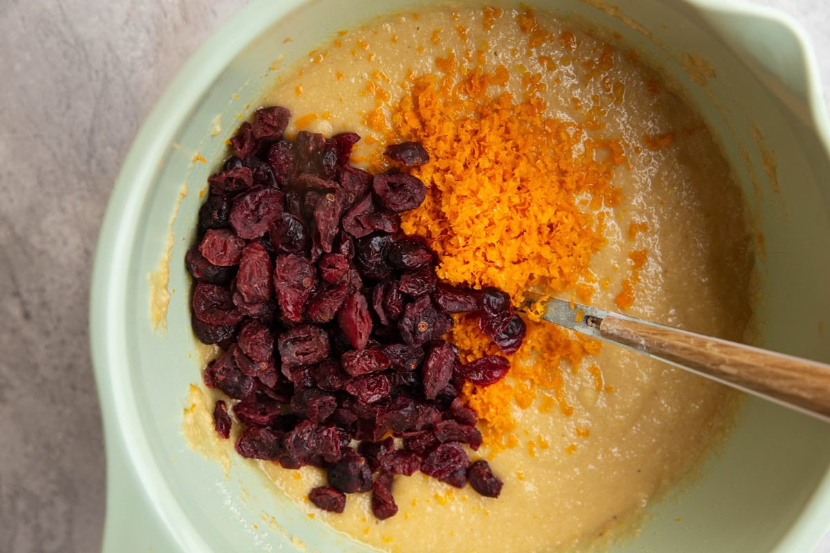 Muffin batter in a large bowl with orange zest and dried cranberries on top, ready to be mixed in.