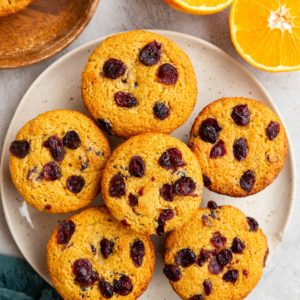 Plate of cranberry orange muffins with a blue napkin and a fresh orange sliced in half to the side.