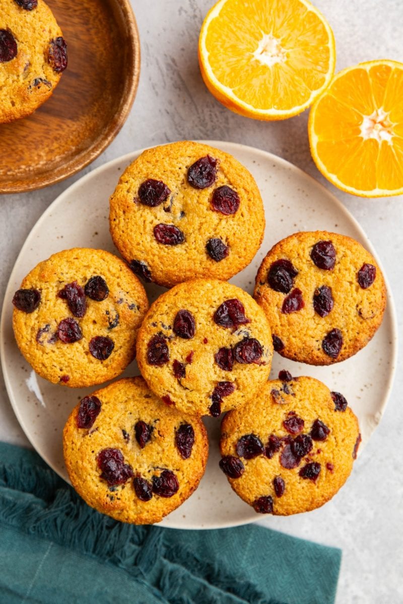 Plate of cranberry orange muffins with a blue napkin and a fresh orange sliced in half to the side.