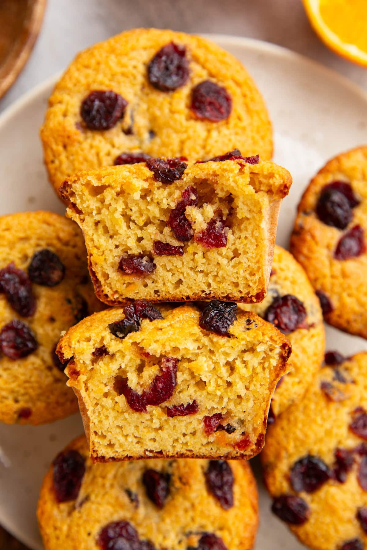 Plate full of cranberry orange muffins with one sliced in half to expose the inside.