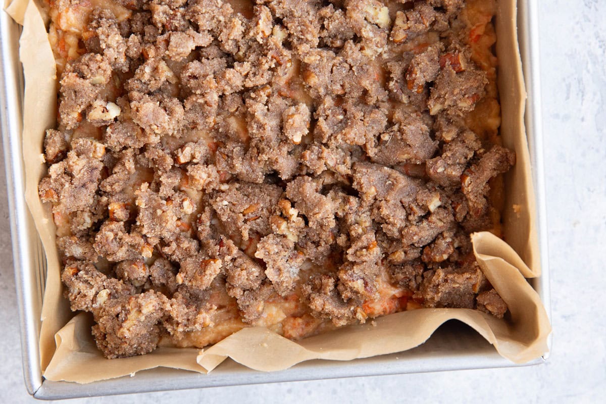 Cake pan with carrot cake batter and coffee cake topping on top, ready to be baked in the oven.