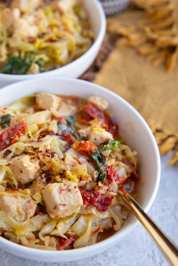 Two white bowls full of cabbage, chicken and creamy sun-dried tomato sauce.