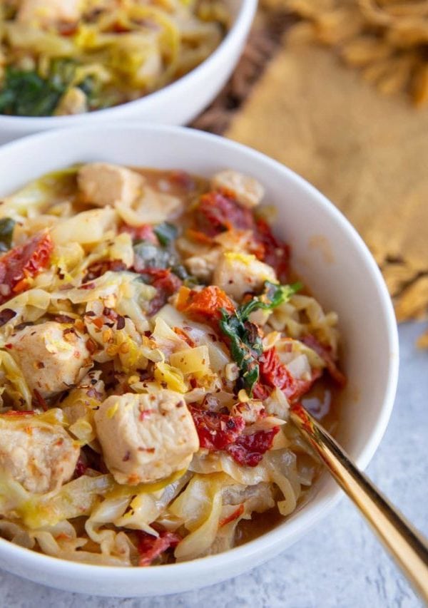 Two white bowls full of cabbage, chicken and creamy sun-dried tomato sauce.